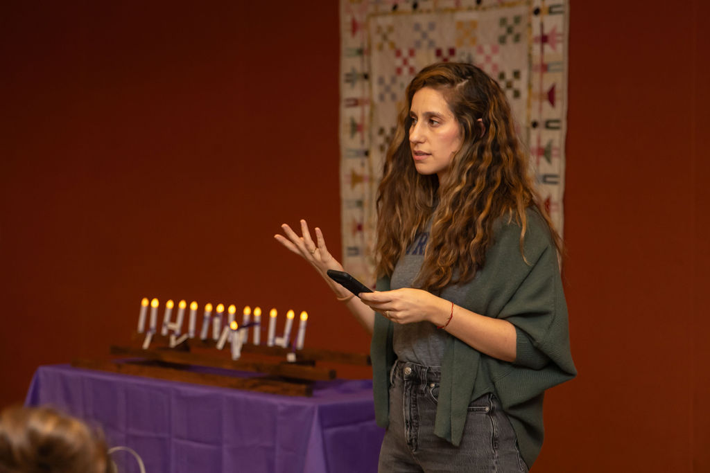 Gina Herrera Pennacchi speaking at a remembrance event, next to a row of candles.